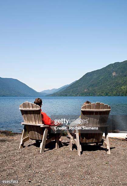 a couple relaxing in wooden chairs near the lake shore. - lago crescent fotografías e imágenes de stock