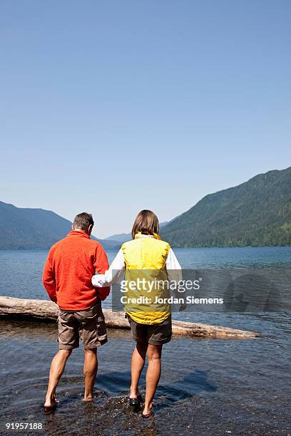 a woman holds a mans arm while walking out to a log in a lake. - lago crescent foto e immagini stock