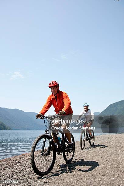 mountain bikers enjoy views of the lake and the hillsides covered in trees while riding along the sh - lago crescent foto e immagini stock