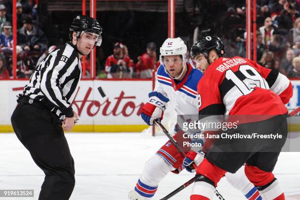 Lineman James Tobias looks on as Derick Brassard of the Ottawa Senators and Peter Holland of the New York Rangers track the puck after a face-off in...