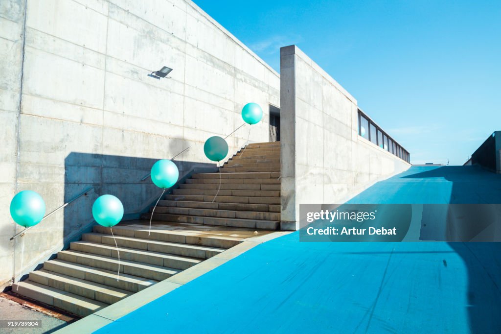Poetic stop motion picture of green balloons following each other going up on stairs in a minimal and cool architecture corner in the city.