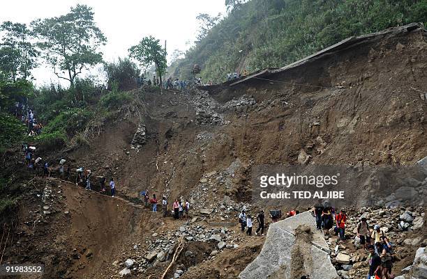 Photo taken on October 12, 2009 shows stranded commuters walking along a footpath below a collapsed highway in the town of Tuba, Benguet province,...