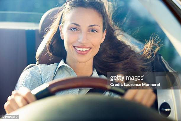 smiling dark-haired woman driving a convertible - mujer conduciendo fotografías e imágenes de stock