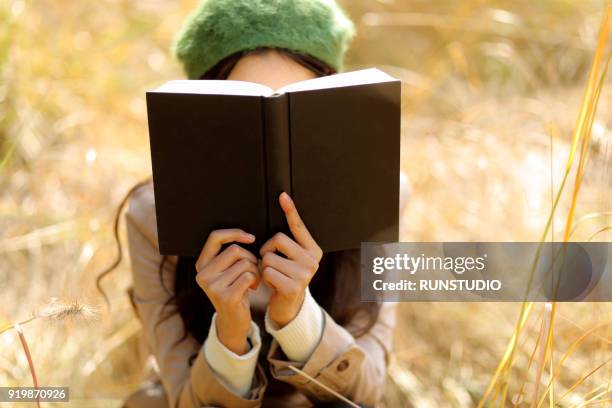 woman covering face with book in autumn park - mujer leyendo libro en el parque fotografías e imágenes de stock