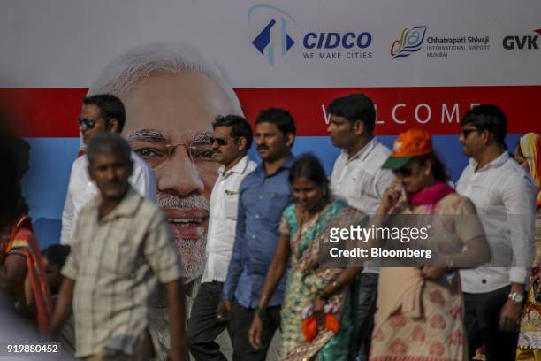 People walk past a billboard depicting Narendra Modi, India's prime minister, on display during a ceremony at the site of the new Navi Mumbai...