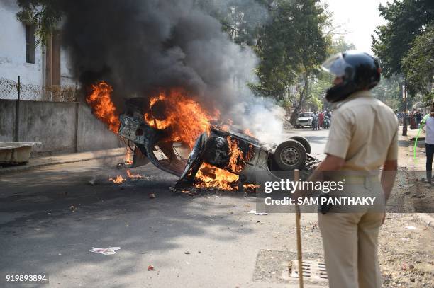 An Indian police officer is seen near a burning car which was set ablaze by a mob in Ahmedabad on February 18, 2018. Protesters torched a car and a...