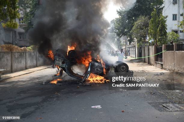 An Indian resident tries to douse the flames of a burning car which was set ablaze by a mob in Ahmedabad on February 18, 2018. Protesters torched a...