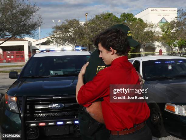 Alfonso Calderon a Junior at Marjory Stoneman Douglas High School hugs Broward County Sheriff officer Brad Griesinger as he guards the front gate of...