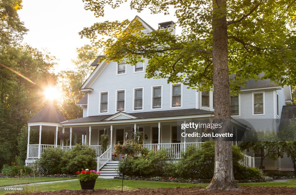 Victorian home with lawn and large front porch in summer at sunset