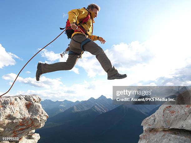 mountaineer jumps gap between rock cliffs - tuffi dalle rocce foto e immagini stock