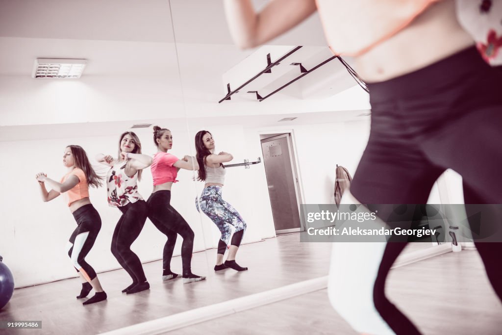 Grupo de giro fêmeas sorrindo treinamento Zumba na frente do espelho no ginásio