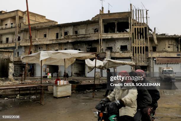 Syrians ride a motorbike past a boy selling cigarettes in the street in Raqa, the former de facto capital of the Islamic State group, on February 18,...