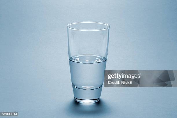 half full water glass over blue background - cup of water stockfoto's en -beelden