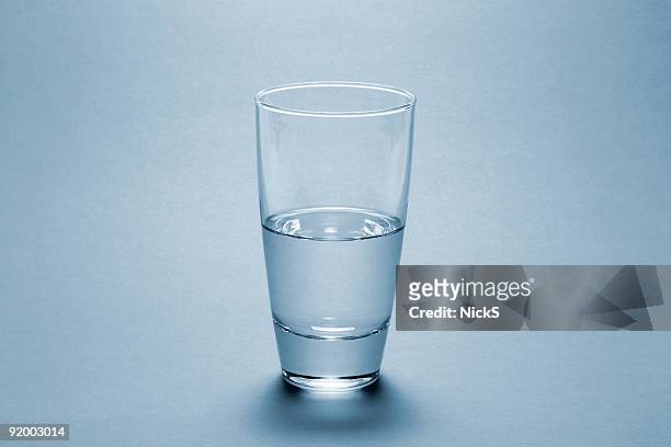 half full water glass over blue background - drinking glass stock pictures, royalty-free photos & images