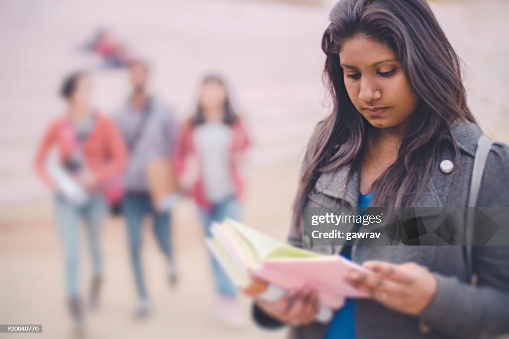 Female college student reading a book in college campus.