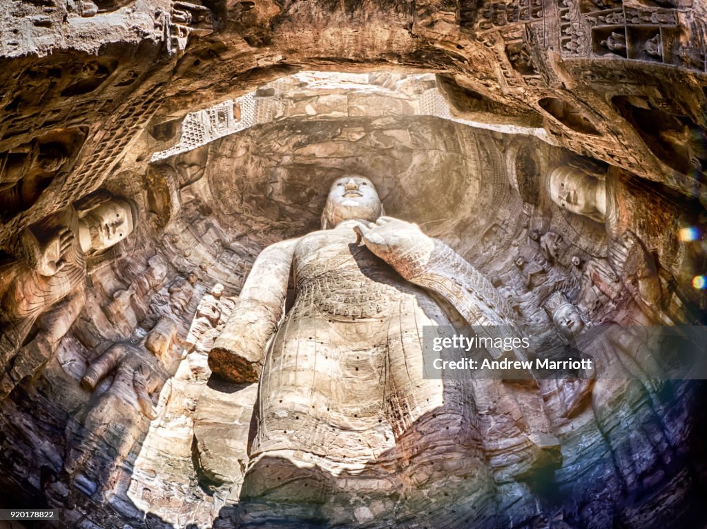 Massive standing Buddha statue in cave full of natural light