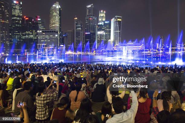 People take photographs as they watch the Spectra light and water show at the Marina Bay waterfront at night in Singapore, on Friday, Feb. 16, 2018....