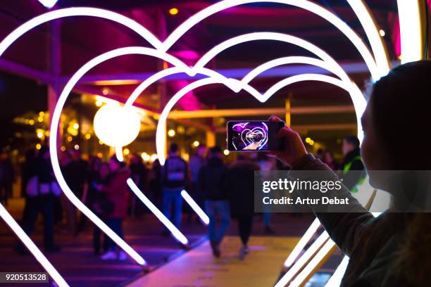 woman with smartphone taking picture of heart shape lights in the city street. - showing smartphone stock pictures, royalty-free photos & images