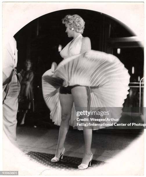 American actress and sex symbol Marilyn Monroe stands on a subway grate as her skirt billows out around her on location during the filming of 'The...