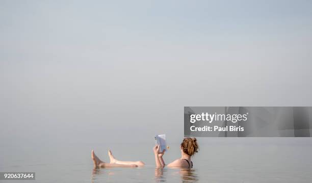 young woman reading a book and  floating on the death sea, jordan. - dead female bodies stock pictures, royalty-free photos & images