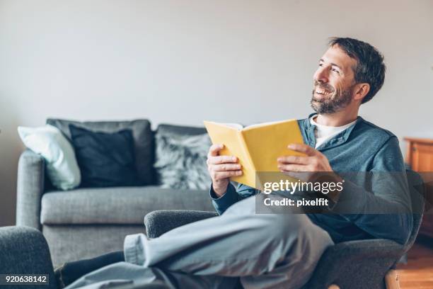 happy middle aged man with a book at home - man hobbies stock pictures, royalty-free photos & images