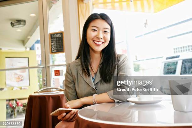 smiling asian businesswoman drinking coffee and holding cell phone - korean ethnicity stock pictures, royalty-free photos & images