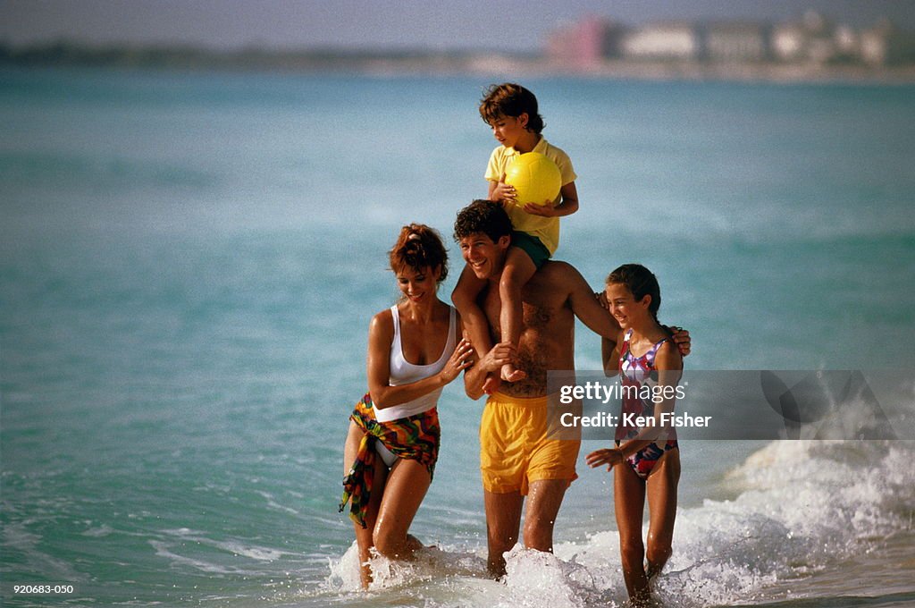 Family of four walking along beach, boy(6-8)on father's shoulders