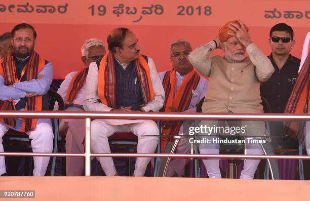 Prime Minister Narendra Modi adjusts his head gear as union minister Ananth Kumar looks on during a political rally at Maharaja Ground ahead of state...