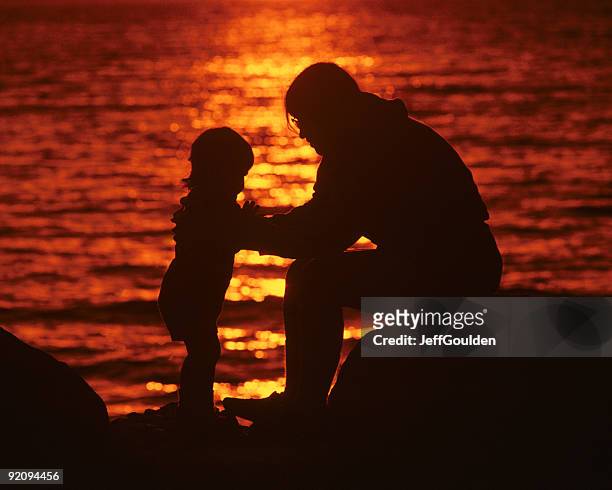 madre e hijas sentarse en la playa al atardecer - jeff goulden fotografías e imágenes de stock