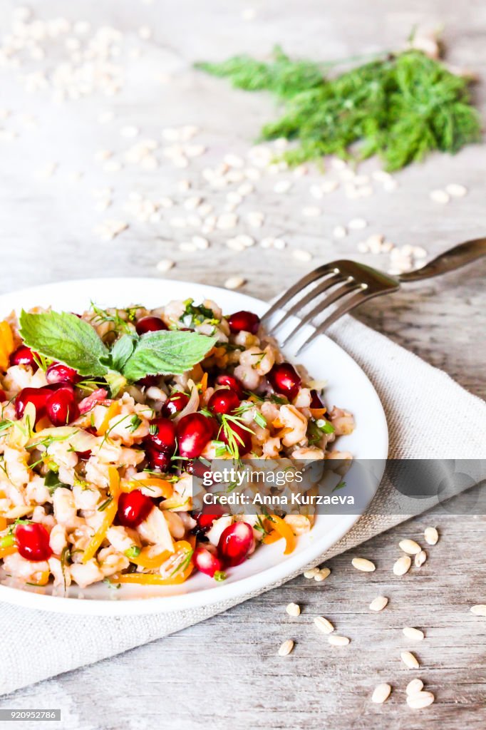 Warm salad with barley, carrot, onion, pomegranate seeds and fresh mint in a plate on a wooden table, selective focus