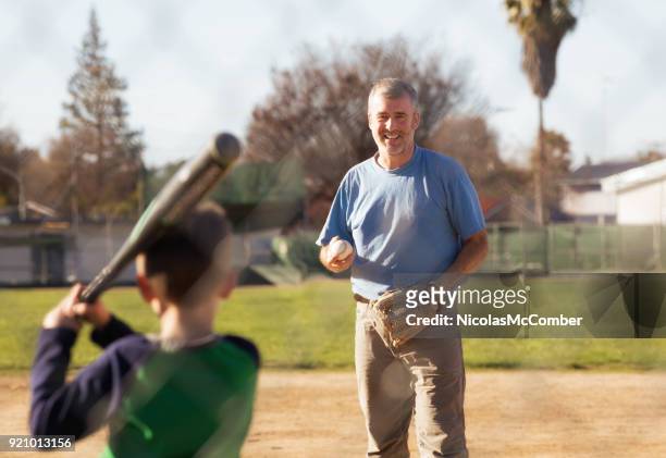 mature father smiling while practicing baseball with young son - throwing baseball stock pictures, royalty-free photos & images