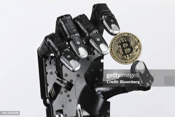 The Shadow Dexterous robotic hand, manufactured by The Shadow Robot Company, holds a coin representing Bitcoin cryptocurrency during a demonstration...