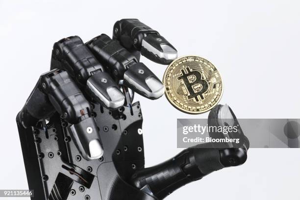 The Shadow Dexterous robotic hand, manufactured by The Shadow Robot Company, holds a coin representing Bitcoin cryptocurrency during a demonstration...