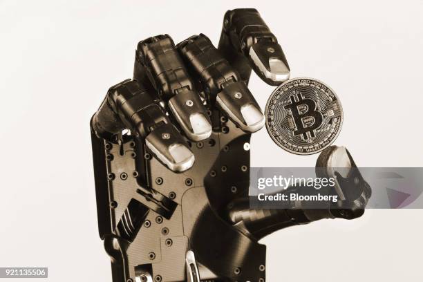 The Shadow Dexterous robotic hand, manufactured by The Shadow Robot Company, holds a coin representing Bitcoin cryptocurrency during a demonstration...