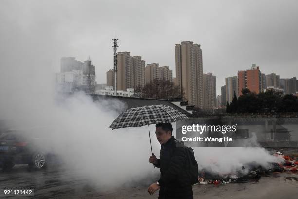 Man holds an umbrella walk in front burning incense at the Guiyuan Temple on February 20, 2018 in Wuhan, Hubei province, China. The fifth day in the...