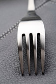 metal fork on black leather place mat, close-up shot