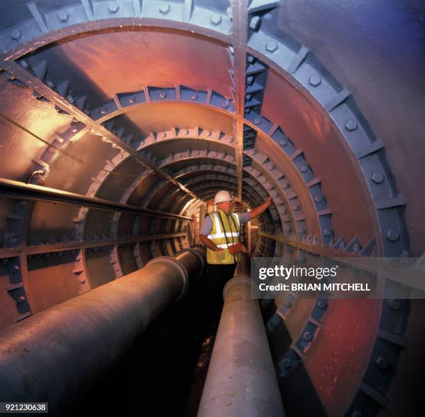 water engineer examining a large underground metal pipe system - rohrleitung stock-fotos und bilder