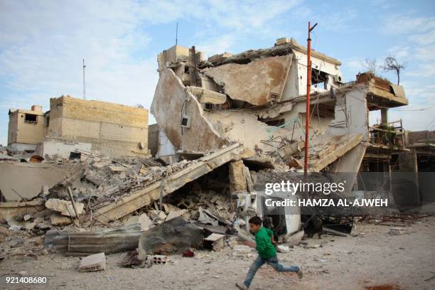 Syrian boy runs past a destroyed building during air strikes by regime forces in the rebel-held town of Douma, in the besieged Eastern Ghouta region...