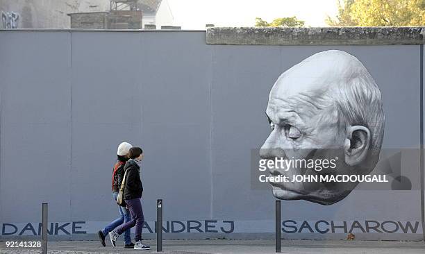 People walk past a painting on the so called East Side Gallery featuring a portrait of Soviet nuclear physicist, dissident and human rights activist...