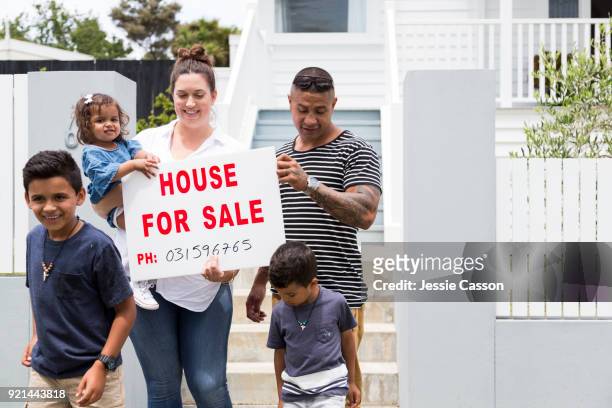 family gather around for sale sign in front of their house - morgage stockfoto's en -beelden