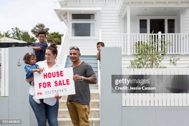 family gather around for sale sign in front of their house - morgage stockfoto's en -beelden