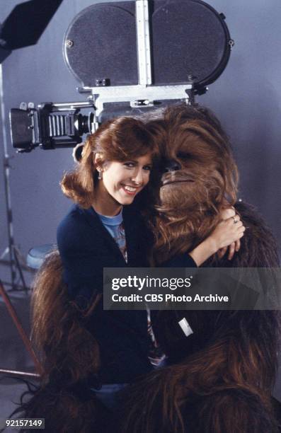 Promotional portrait of American actress Carrie Fisher as she sits on the lap of British actor Peter Mayhew, in costume as Chewbacca, on the set of...