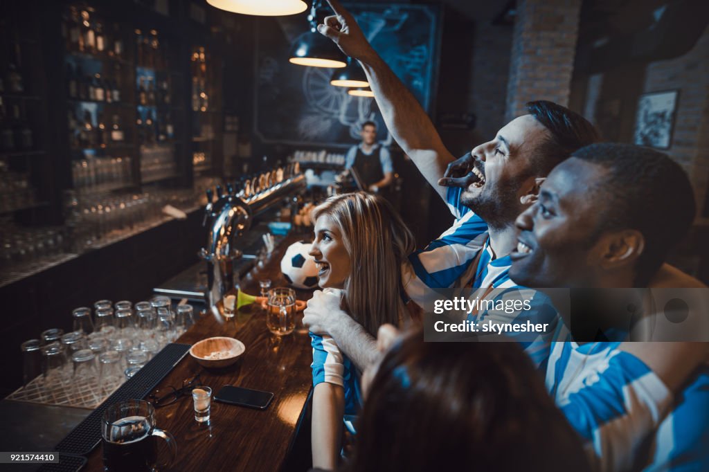 Happy friends enjoying while cheering for their soccer team in a bar.