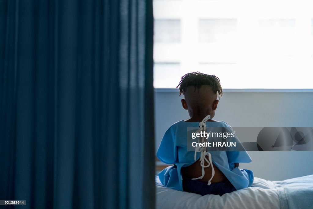 Rear view of boy sitting on bed at hospital