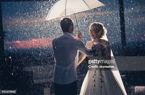 happy newlyweds having fun under the umbrella on a rainy day. - europe bride stock pictures, royalty-free photos & images