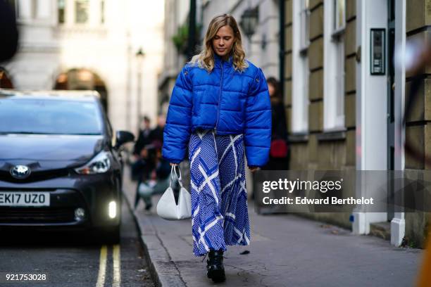 Guest wears a blue puffer coat with a blue skirt and a white bag, during London Fashion Week February 2018 on February 16, 2018 in London, England.