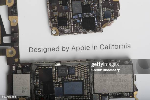 The logic board, bottom, of an Apple Inc. IPhone 6 smartphone sits on a box that reads 'Designed by Apple In California' in an arranged photograph in...
