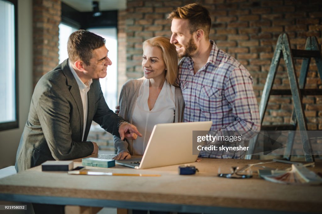 Feliz pareja contratista y jóvenes comunicando durante el uso de computadoras en sitio de construcción del edificio.