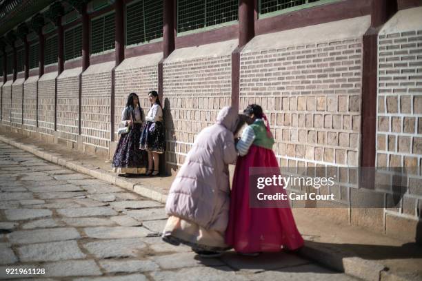 Women wearing traditional Korean Hanbok dresses chat and check photographs on their phones as they visit Gyeongbokgung Palace on February 21, 2018 in...