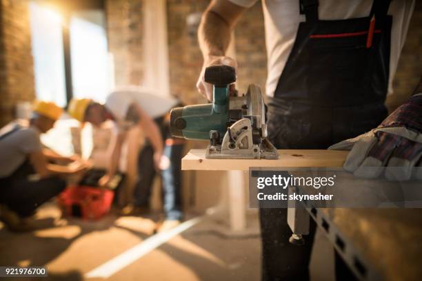 unrecognizable worker cutting plank with circular saw at construction site. - plank house stock pictures, royalty-free photos & images